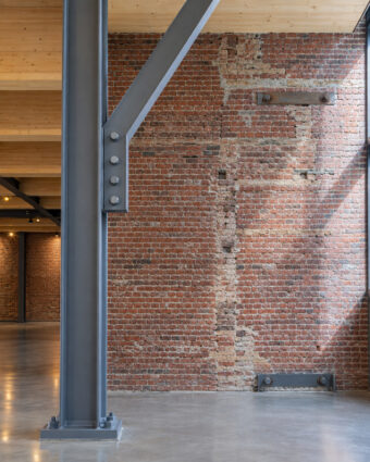 A braced steel frame standing free inside an unreinforced brick shell, under a new glue-laminated floor deck.