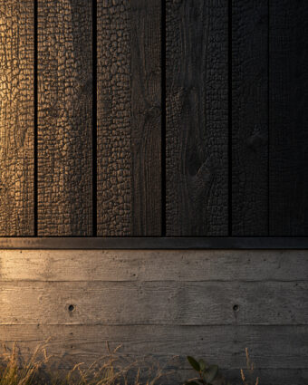 Charred cedar boards meeting board-formed concrete across a shadow reveal, in raking light.