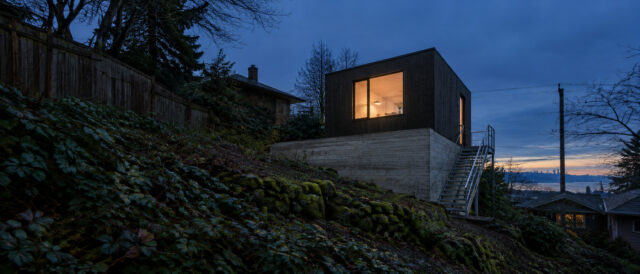 North Slope Studio on its board-formed base, seen from the foot of the slope at dusk.