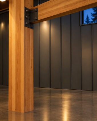 A glue-laminated fir column and beam meeting a blackened steel plate, above a polished concrete floor.
