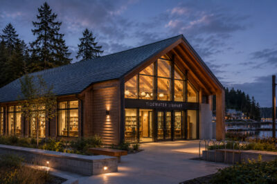 Tidewater Library at dusk, the glazed gable lit from within, harbor beyond.