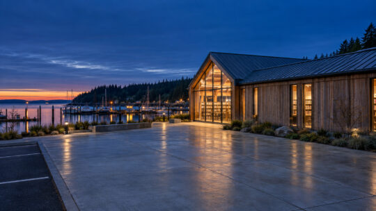 The library across its forecourt at dusk, the glazed north gable lit from within above the harbor.